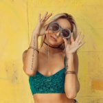 woman in blue bralette holding sunglasses putting on her eyes