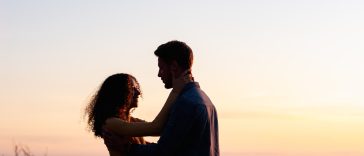 man and woman standing near body of water during sunset