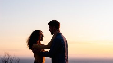 man and woman standing near body of water during sunset